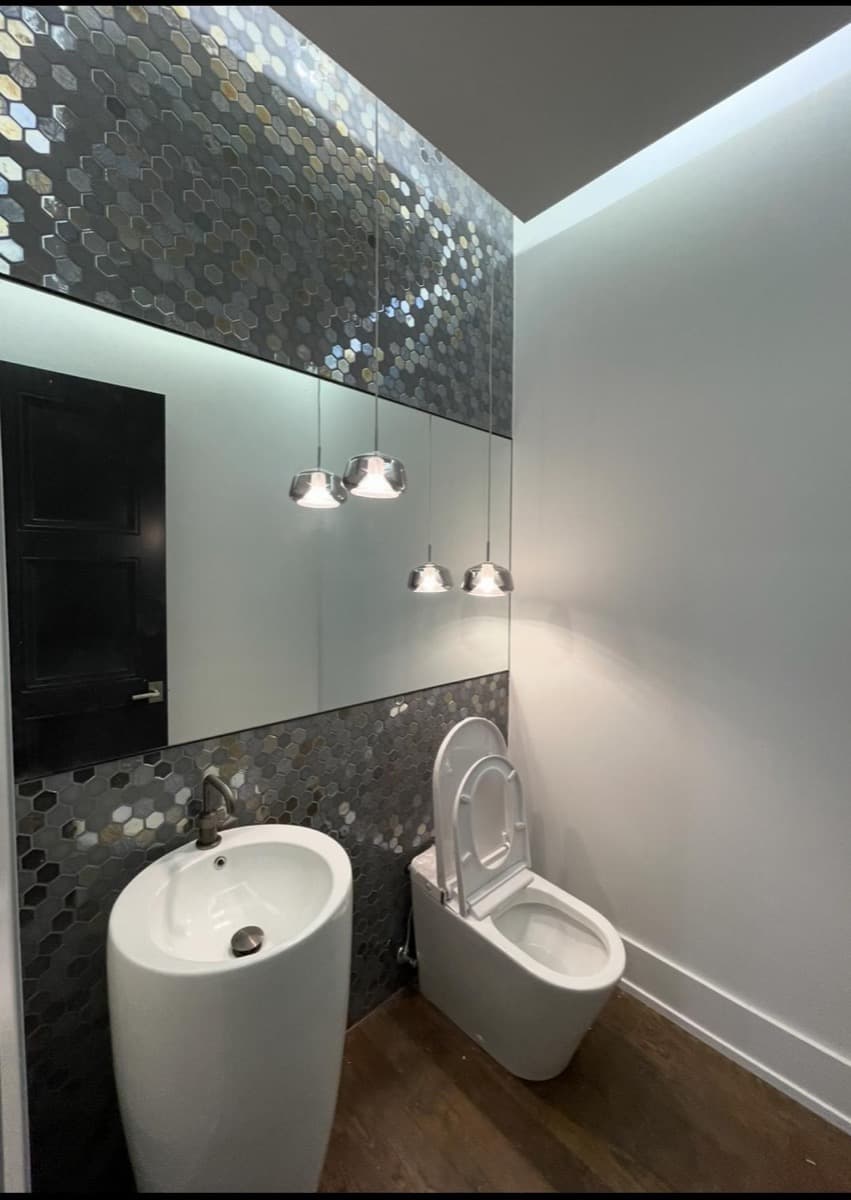Designer powder room with metallic hexagonal accent tile, wall-mounted bidet, and chrome pendant trio